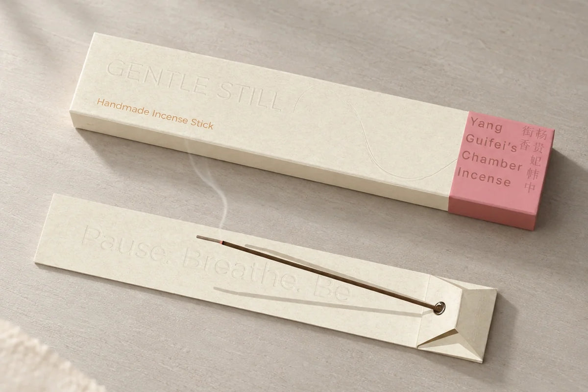 Gentle Still Yang Guifei’s Chamber Incense burning beside its ivory and rose packaging.
